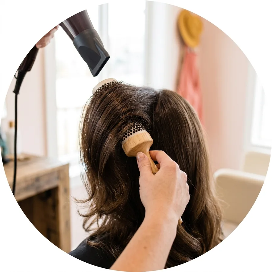 A round brush lifting glossy blown-out hair at the crown